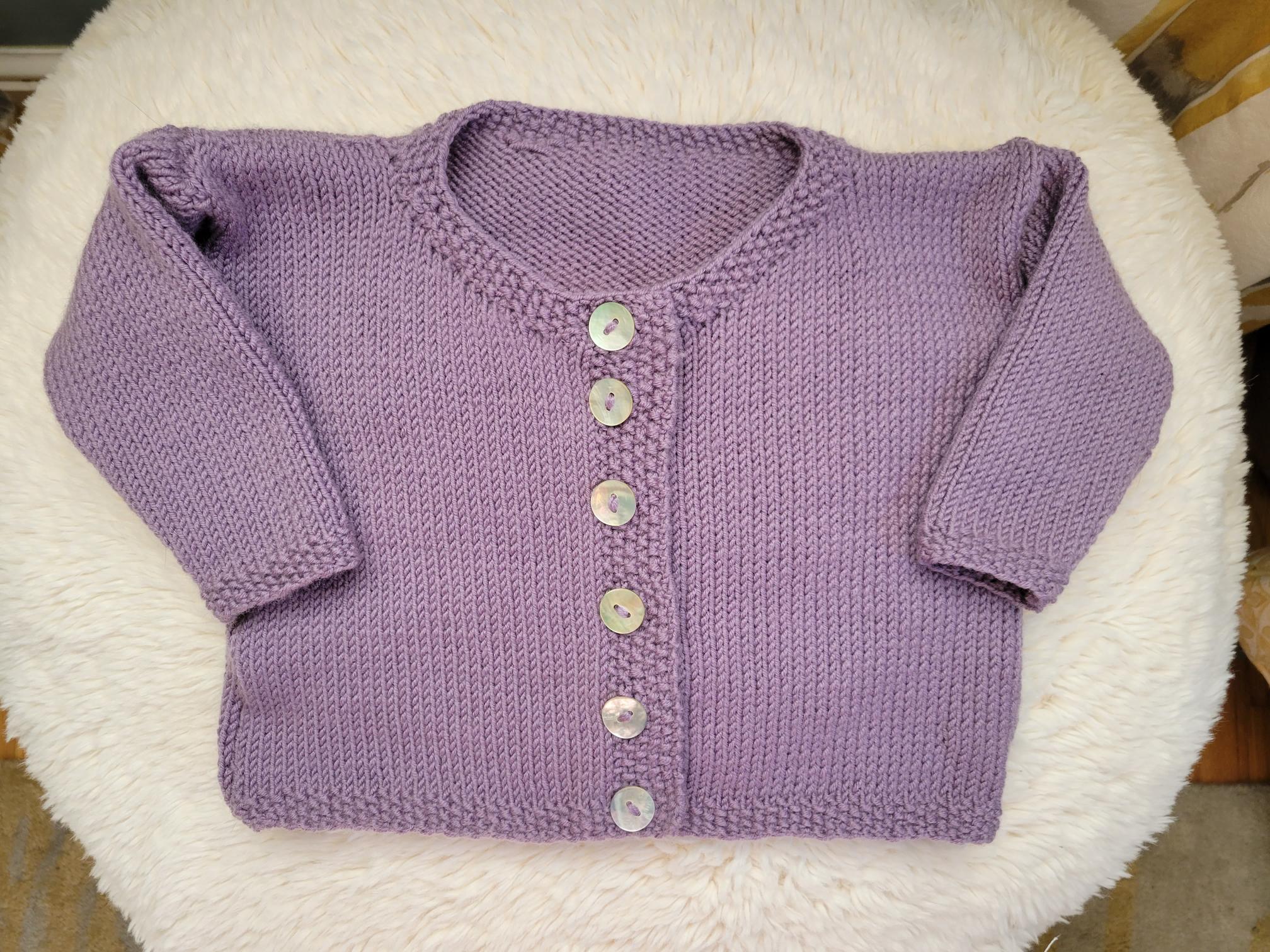 a handknit, lilac-colored baby sweater with shell-colored buttons